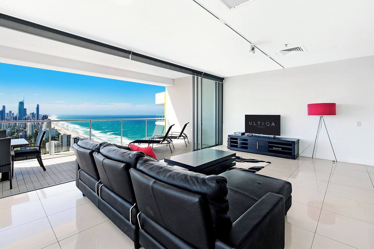A modern living room with a black leather sofa, a TV, and a red floor lamp.