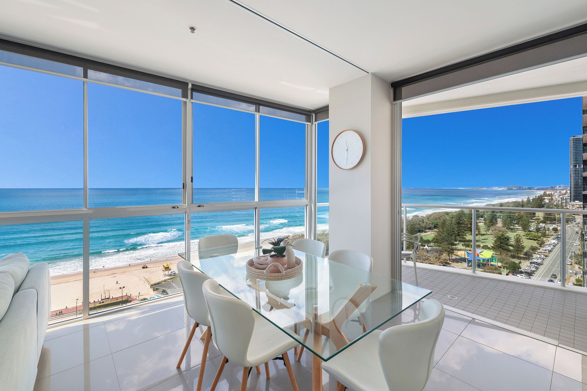 A modern room with a glass table, white chairs, and a view of the ocean.