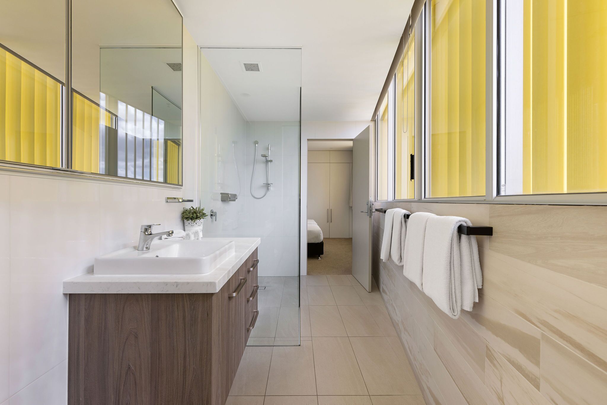 A modern bathroom with a glass shower enclosure, a wooden vanity, and a large mirror.