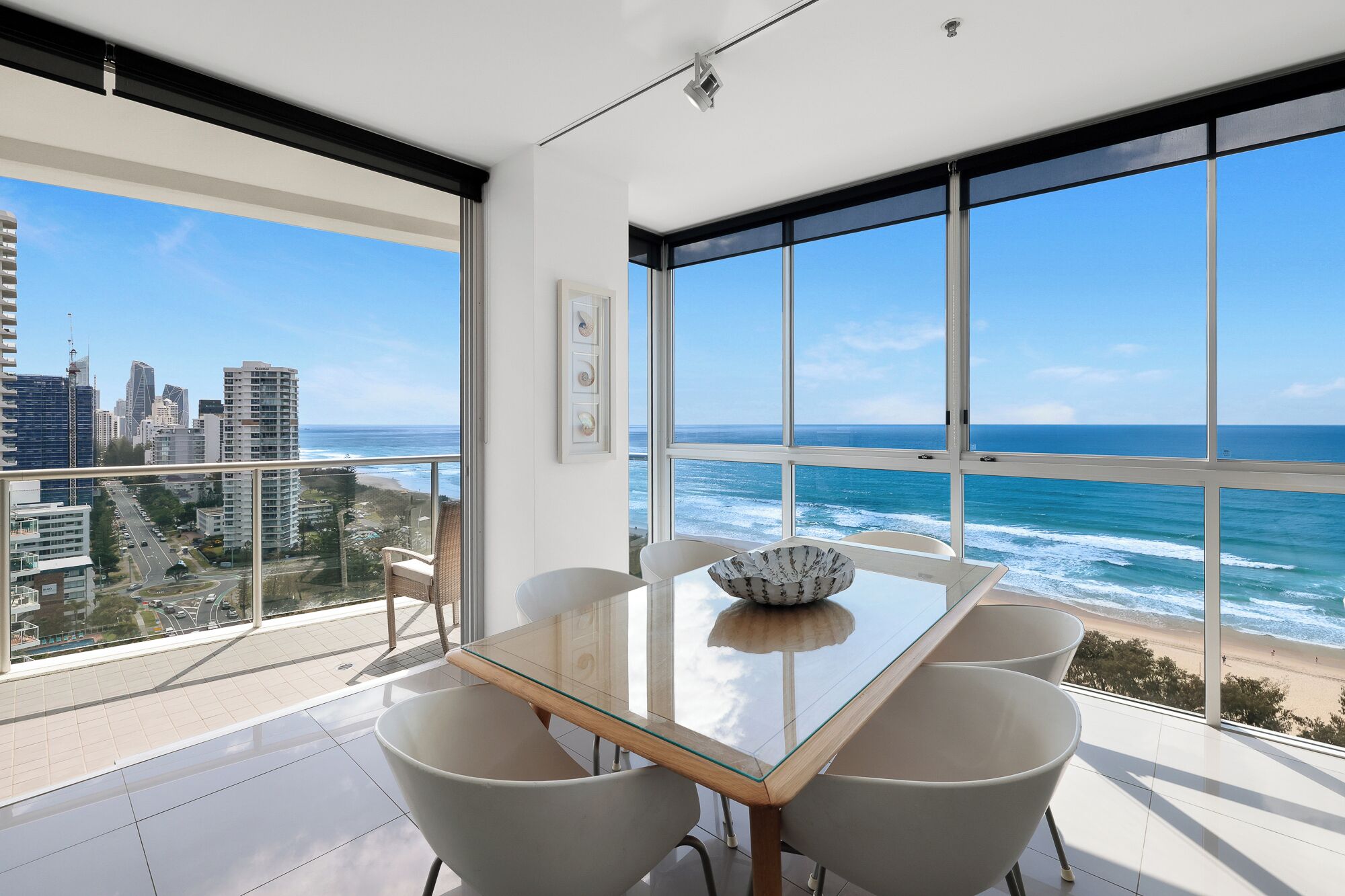 Ein moderner Essbereich mit Glastisch und vier Stühlen, mit Blick auf Stadt und Meer.