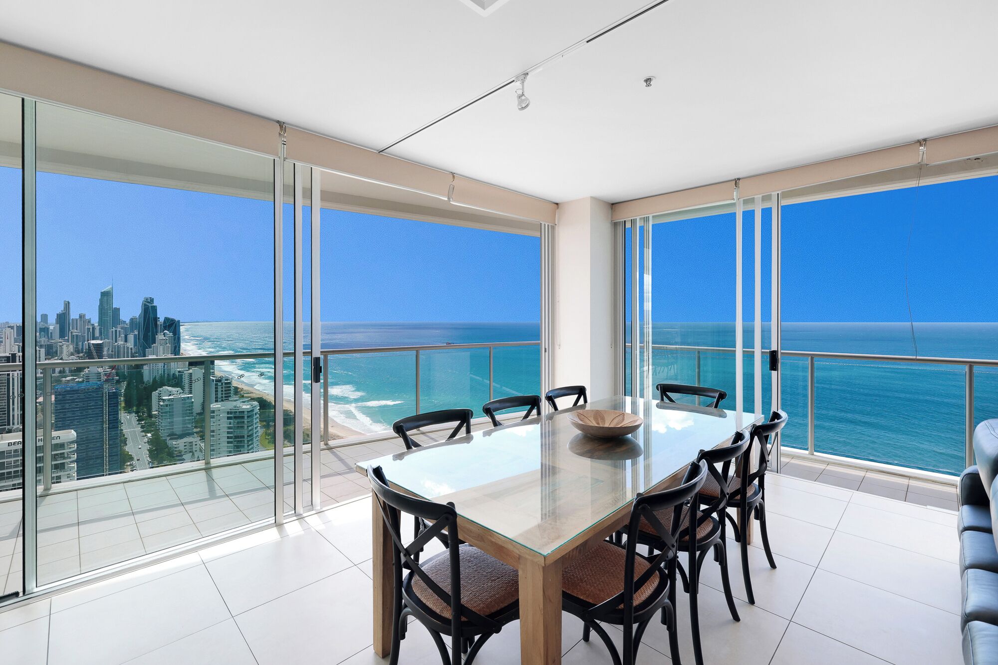 A spacious balcony with a glass table and chairs, offering a view of the city skyline and ocean.