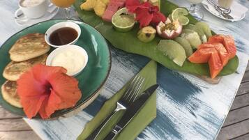 Una mesa de desayuno con diversos alimentos, como panqueques, frutas y bebidas.