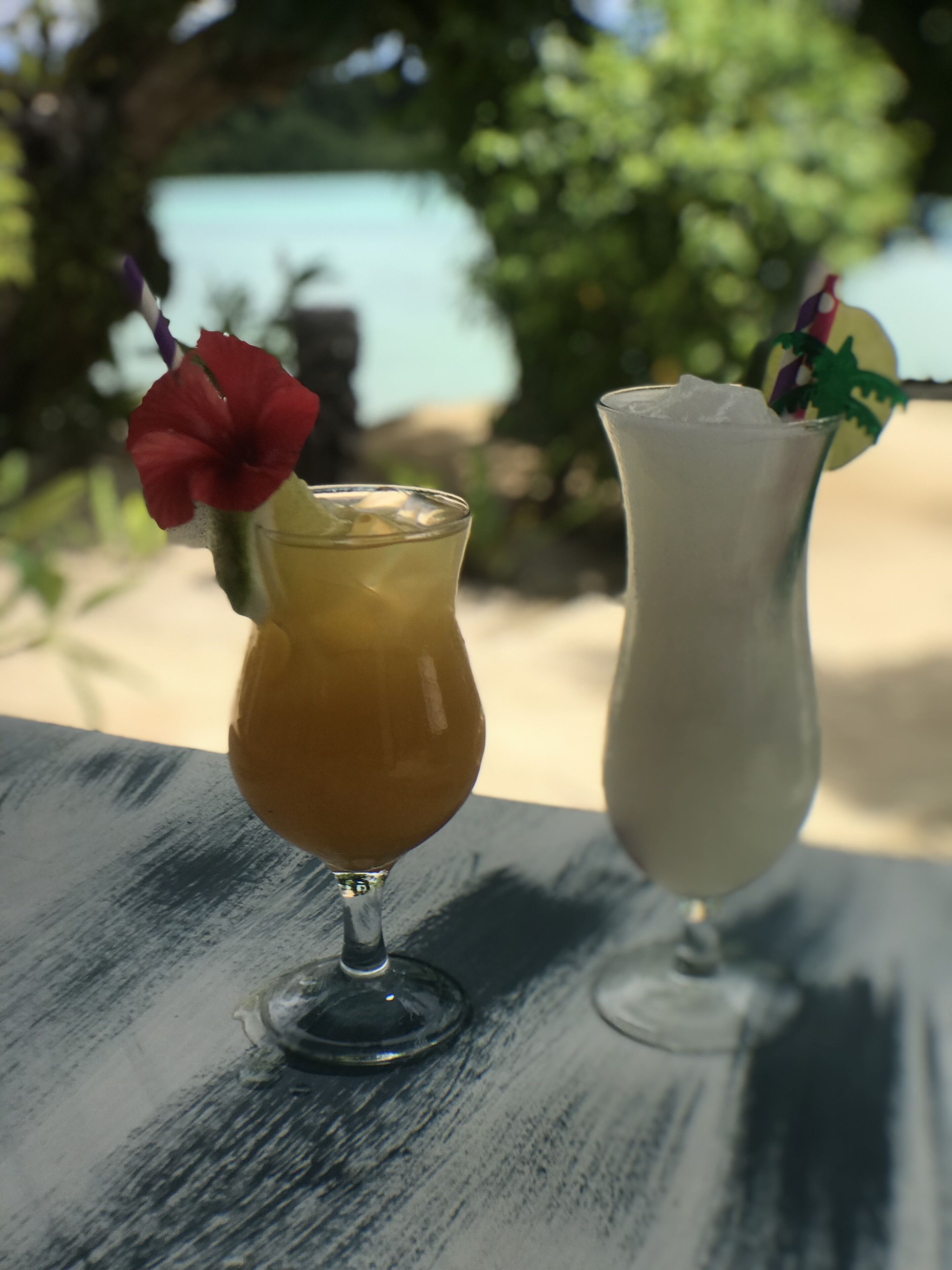 Two drinks on a table with a beach view in the background.