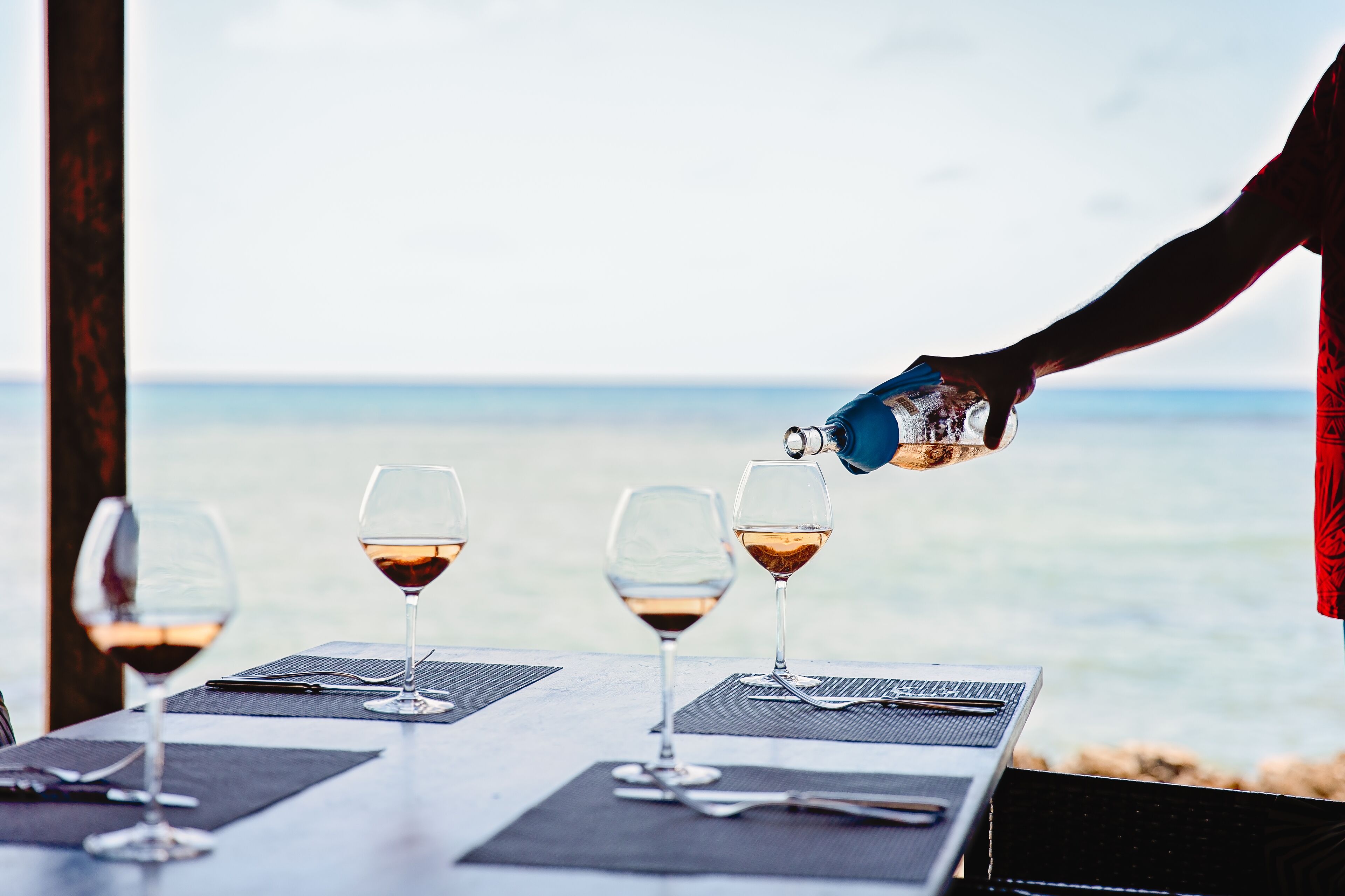 Una mesa con cuatro copas de vino y una persona sirviendo vino en una de ellas.