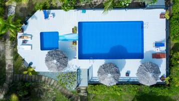 An aerial view of a resort with a large swimming pool, sun loungers, and tropical landscaping.