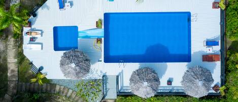 An aerial view of a resort with a large swimming pool, sun loungers, and tropical landscaping.