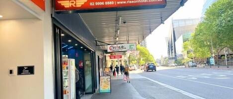 The Sydney Riseon Hotel with a prominent sign, a covered walkway, and a view of the street with cars and pedestrians.