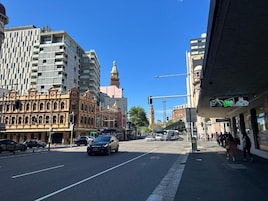 Vista da rua com mistura de edifícios modernos e históricos, céu azul claro e faixa de pedestres.