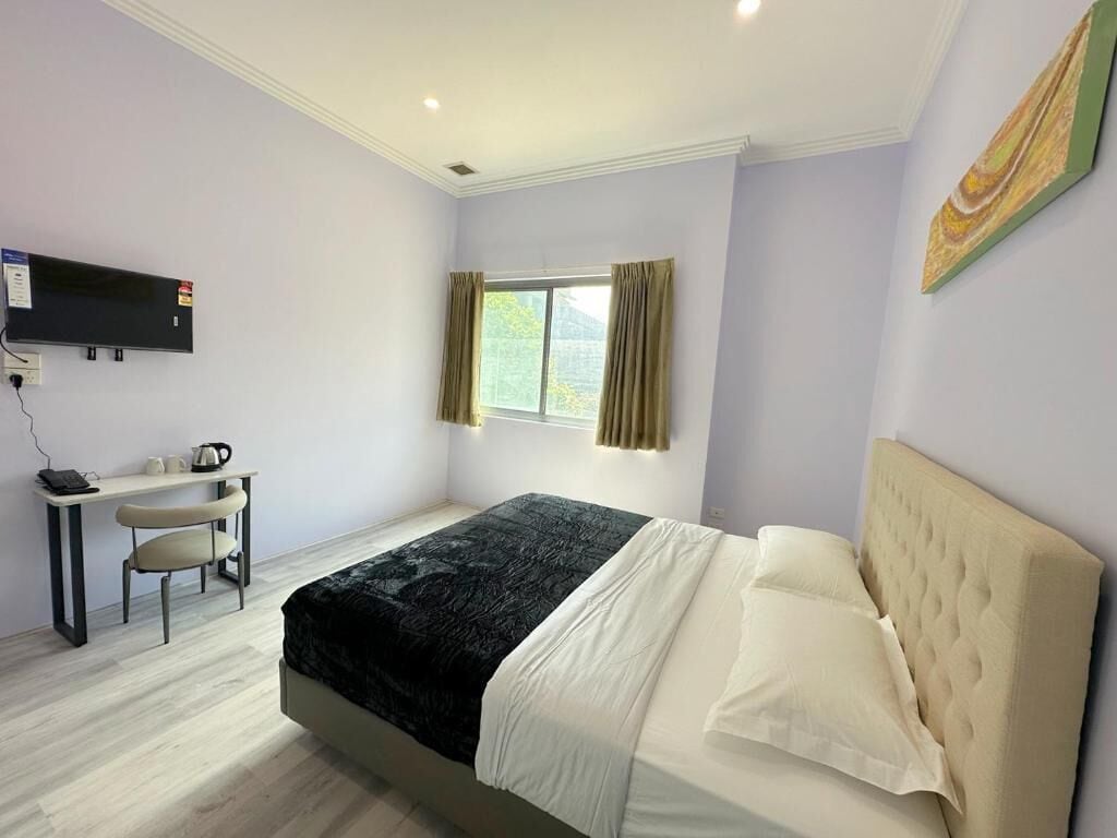 A bedroom with a bed, a desk, a chair, a TV, and a window with curtains.