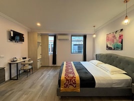 Quarto com cama, escrivaninha e cadeira. Há uma janela com cortinas, um quadro na parede e uma luminária no teto.