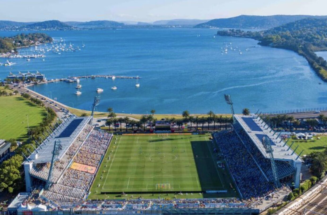 Un estadio con un campo de fútbol rodeado de zonas de asientos y un cuerpo de agua al fondo.