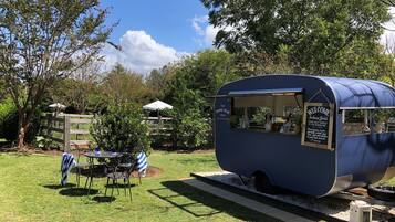 Ein blauer Food-Truck mit dem Schild 'The Pool Bar', geparkt auf einer Rasenfläche, in deren Nähe sich ein Tisch und Stühle befinden.