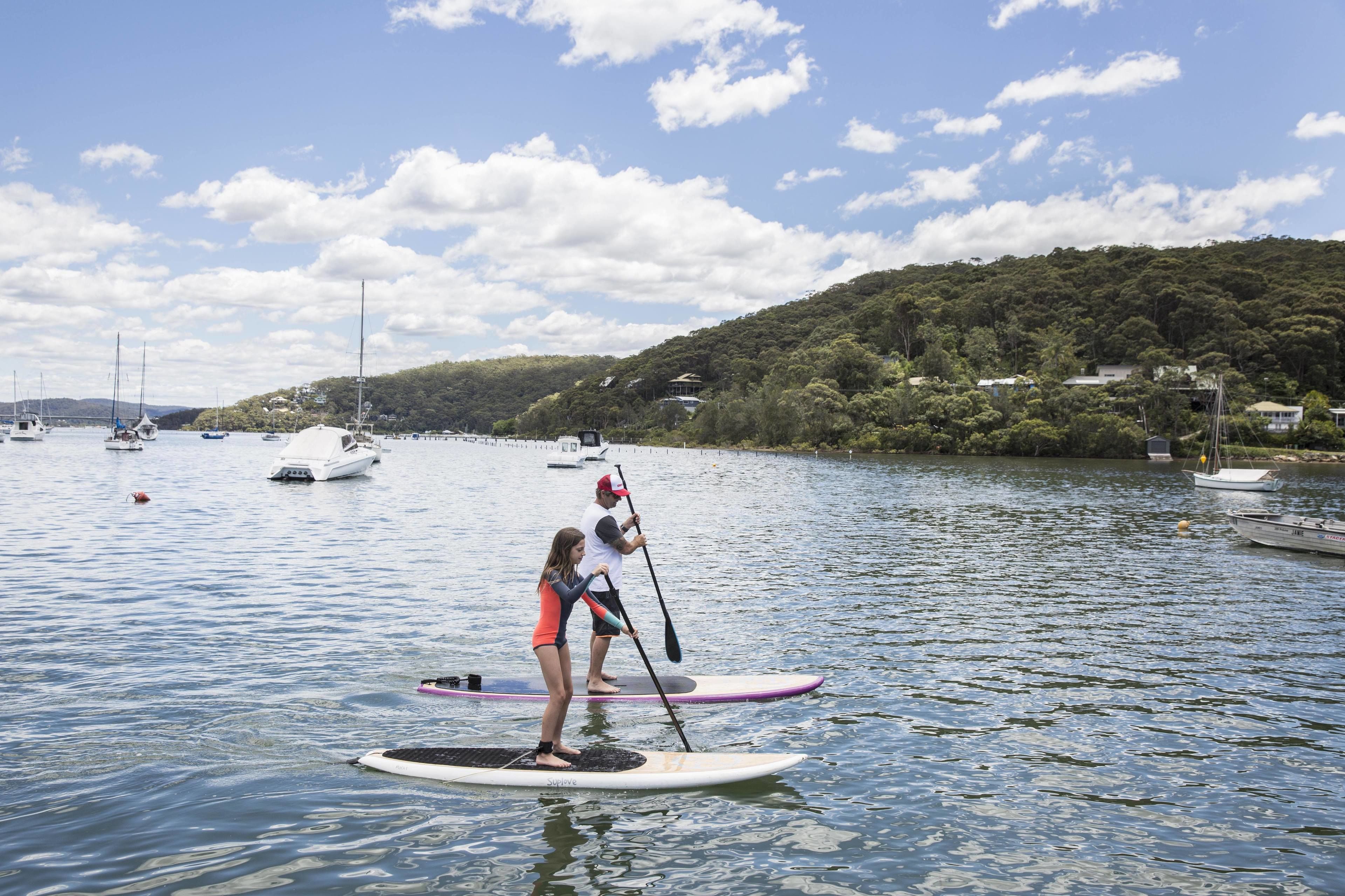 A calm lake with paddleboards, boats, and a hilly landscape in the background.