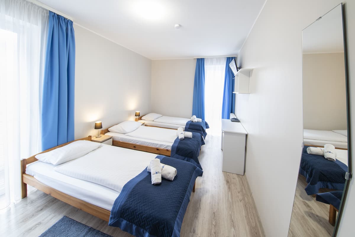 A hotel room with three beds, a desk, and a mirror.