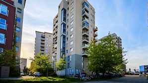 Un edificio residencial alto con varios balcones, rodeado de vegetación y vehículos estacionados.