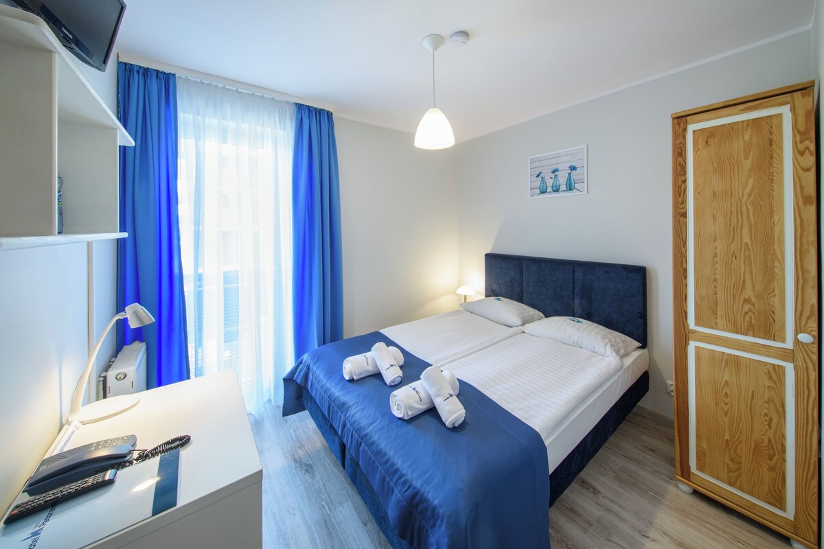 A neatly arranged hotel room with a bed, a wardrobe, a desk with a lamp, and a television.