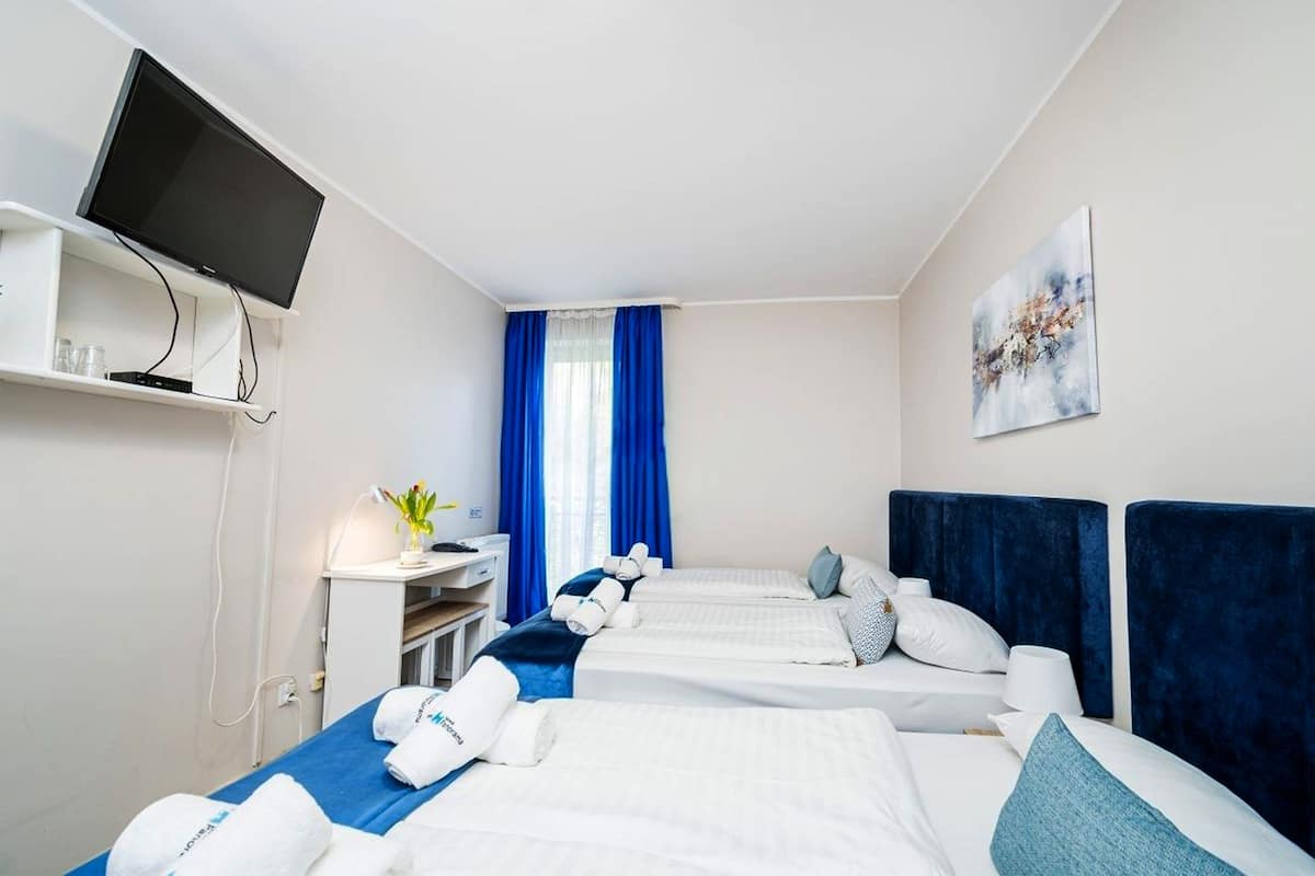 A hotel room with two beds, a desk, a television, and a painting on the wall.