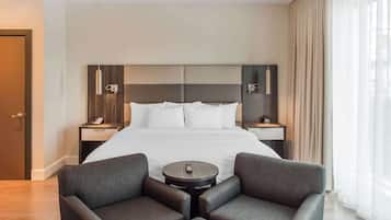 A hotel room with a large bed, two bedside tables, a small round table, and two armchairs.