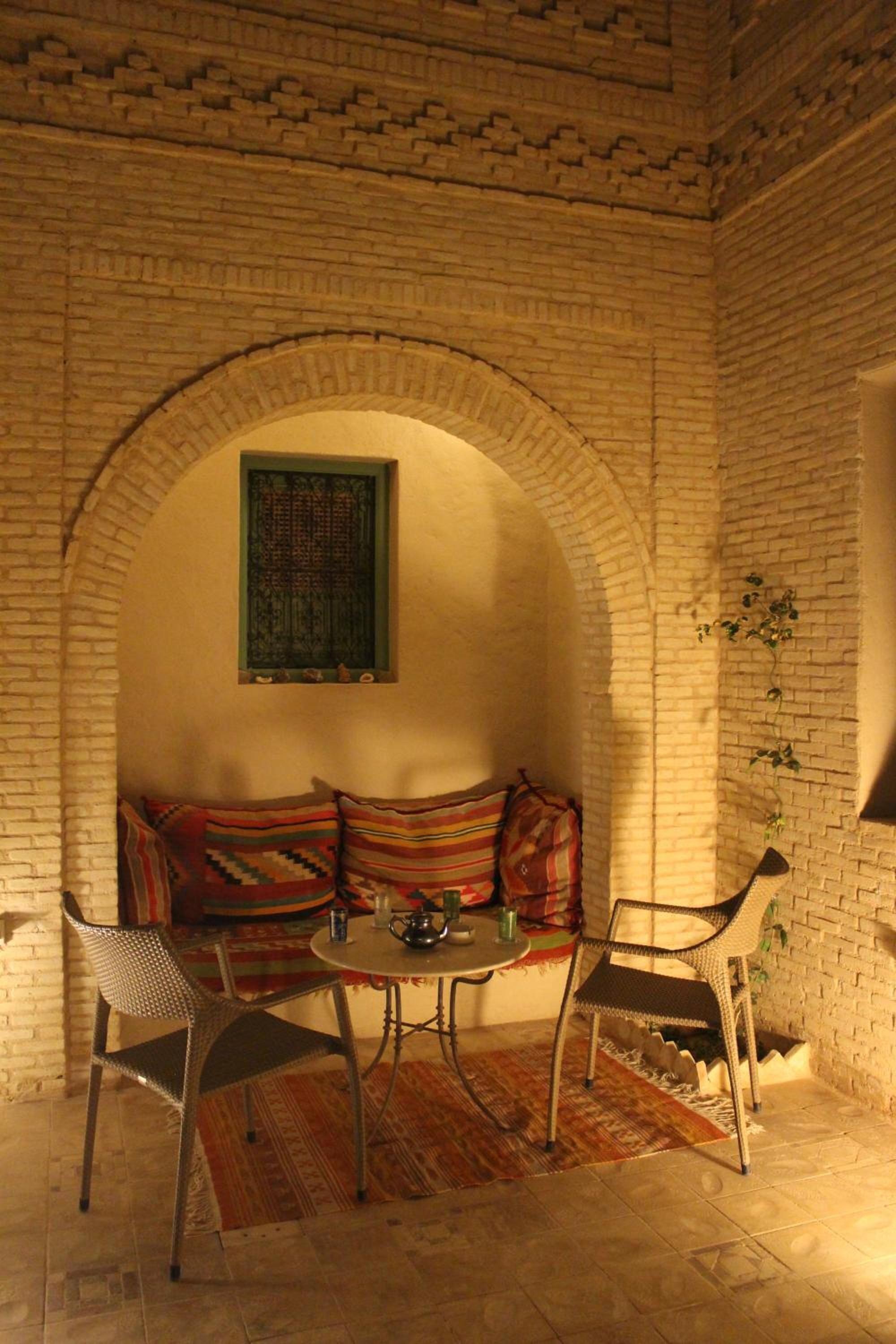 A cozy seating area with a cushioned bench, two metal chairs, a small round table, and a patterned rug.