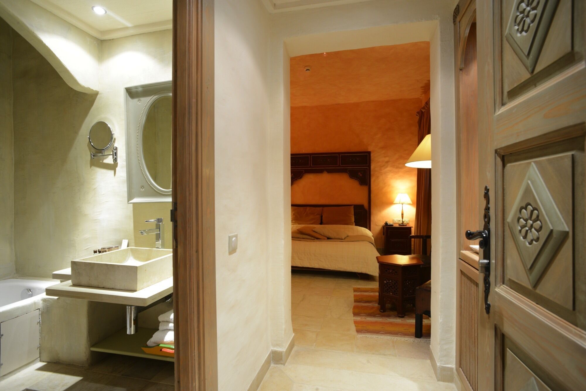 Una camera d'albergo con bagno, un letto, un comodino e una lampada.