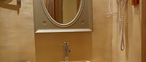 A bathroom with a rectangular sink, a mirror with a decorative frame, a hairdryer mounted on the wall, and a towel rack.