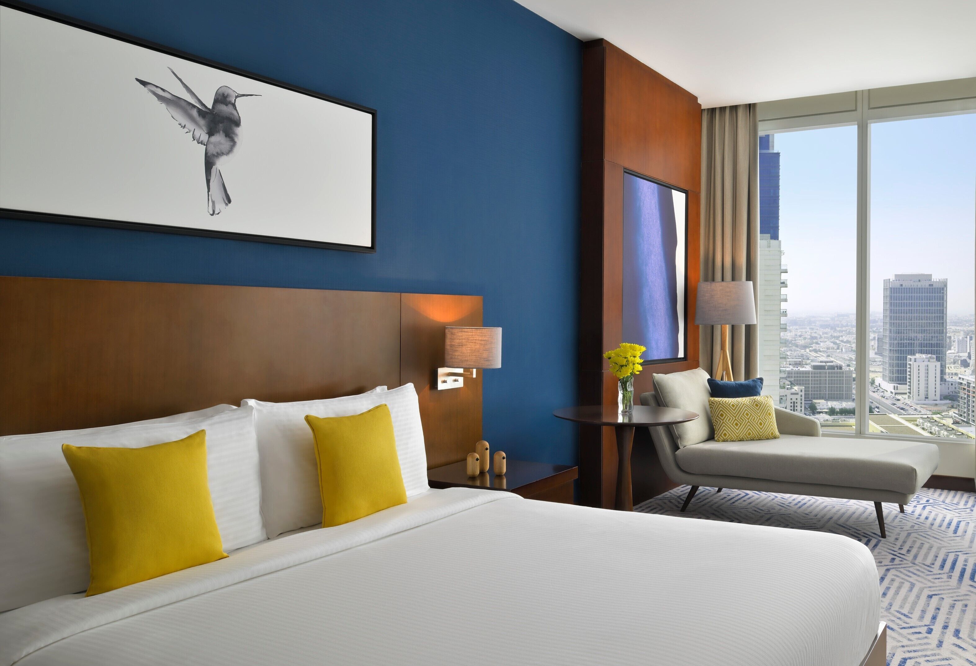 Habitación de hotel con una cama grande, un escritorio, una silla y un ventanal con vistas a la ciudad.