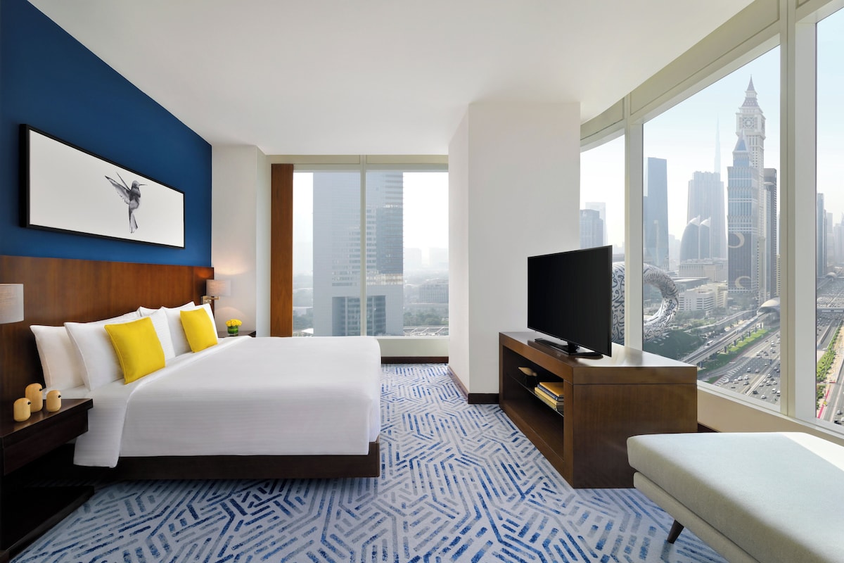 A modern hotel room with a large bed, a flat-screen TV, and a city view.