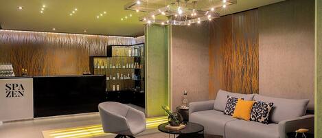 A modern interior with a sofa, chairs, a coffee table, a decorative light fixture, and a reception desk.