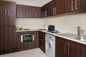 A modern kitchen with wooden cabinets, a dishwasher, a washing machine, and a sink.