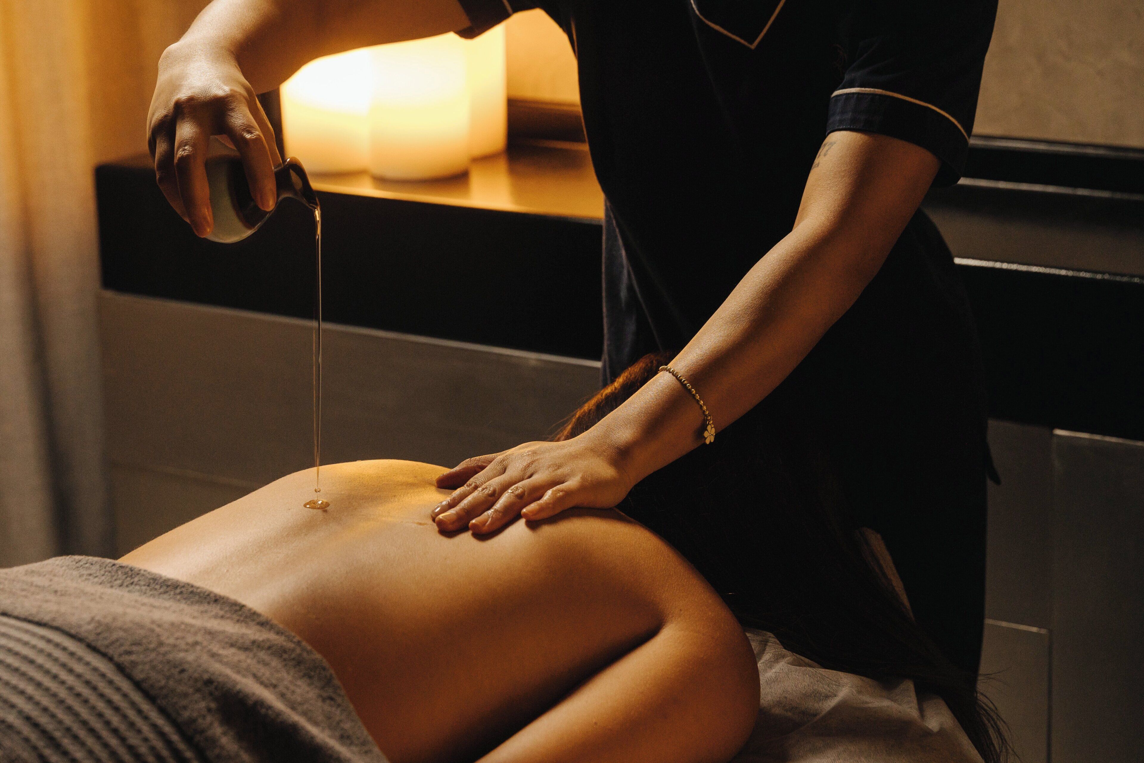 Une personne effectue un massage sur une autre, avec une bougie et une table de massage en arrière-plan.