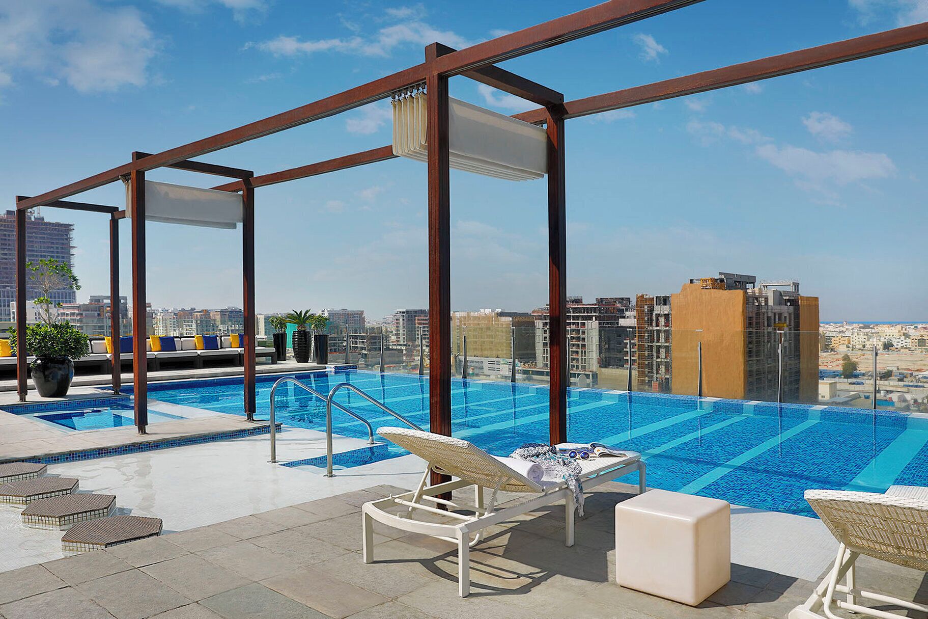 A rooftop infinity pool with lounge chairs and a city view.