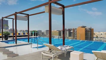 A rooftop infinity pool with lounge chairs and a city view.
