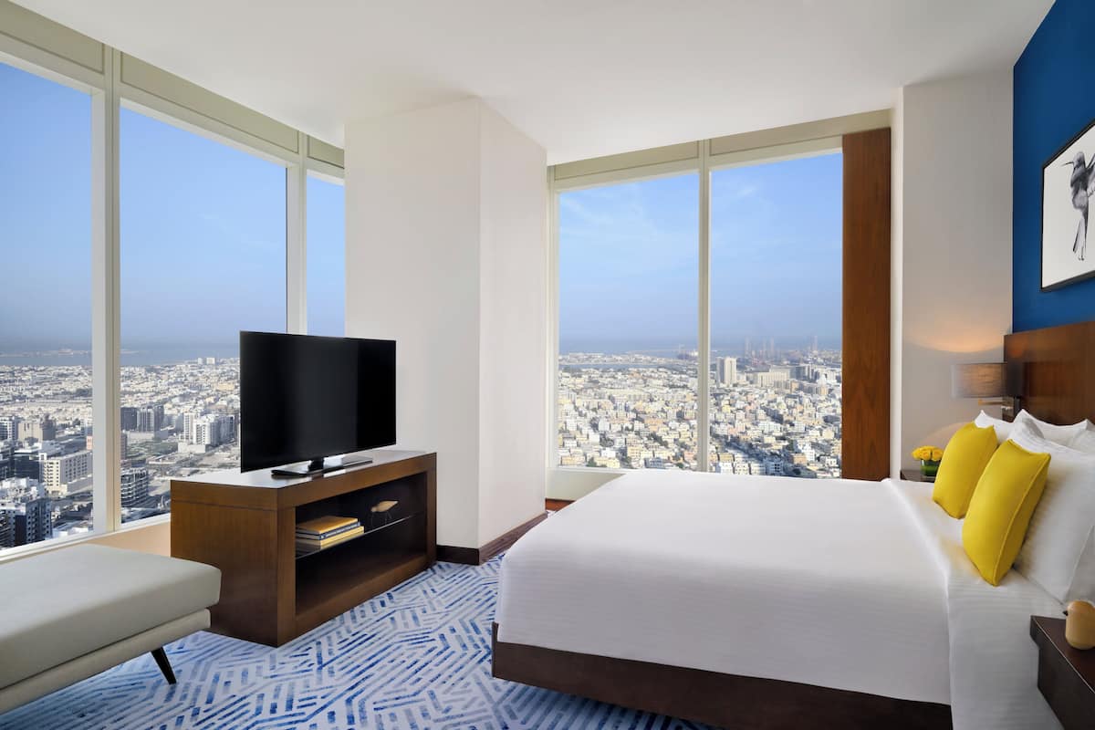 A hotel room with a large bed, a television, and a view of a cityscape.