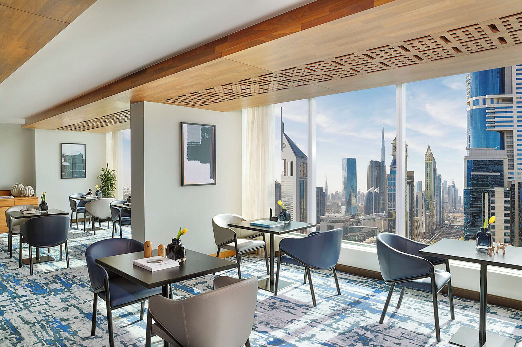 A hotel room with a city view, a dining area, and a seating area with a patterned carpet.