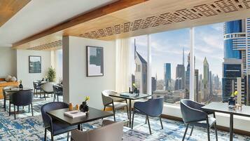 A hotel room with a city view, a dining area, and a seating area with a patterned carpet.