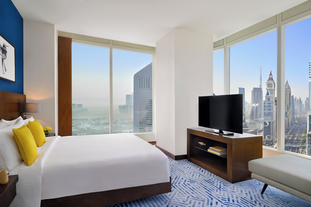 A hotel room with a large bed, a TV, and a city view.