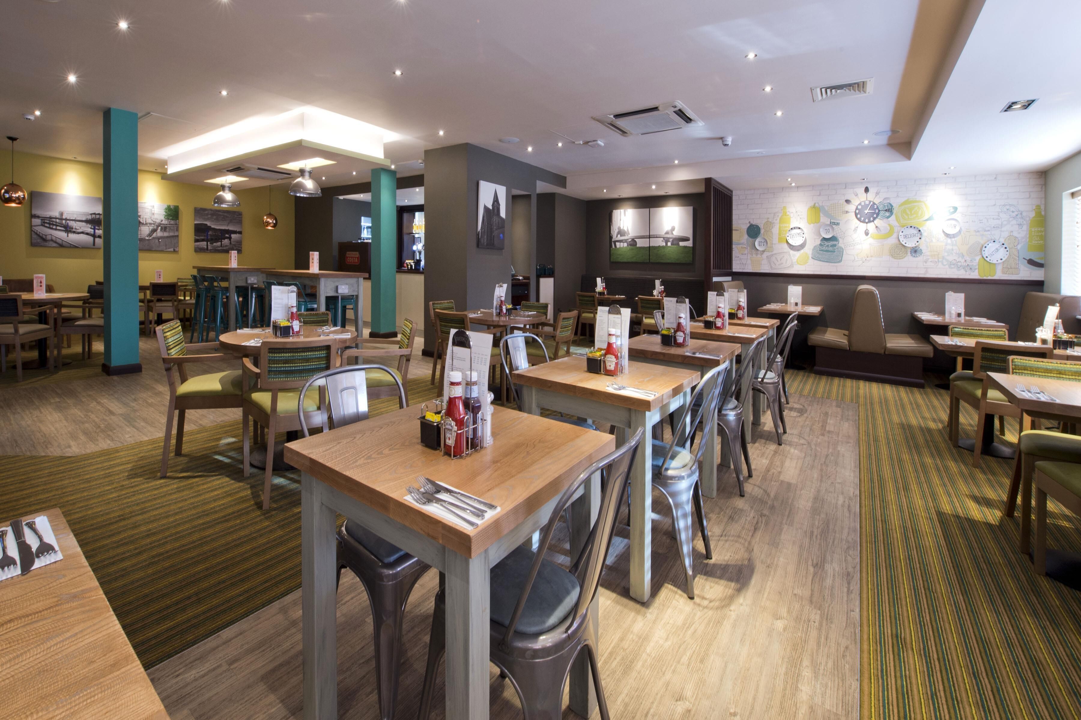 A restaurant with multiple tables and chairs, a counter, and a wall with clocks and bottles.