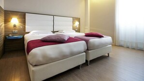 Une chambre d’hôtel avec deux lits, une tête de lit en bois, des lampes de chevet et une grande fenêtre avec des rideaux.