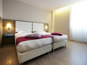 Une chambre d’hôtel avec deux lits, une tête de lit en bois, des lampes de chevet et une grande fenêtre avec des rideaux.
