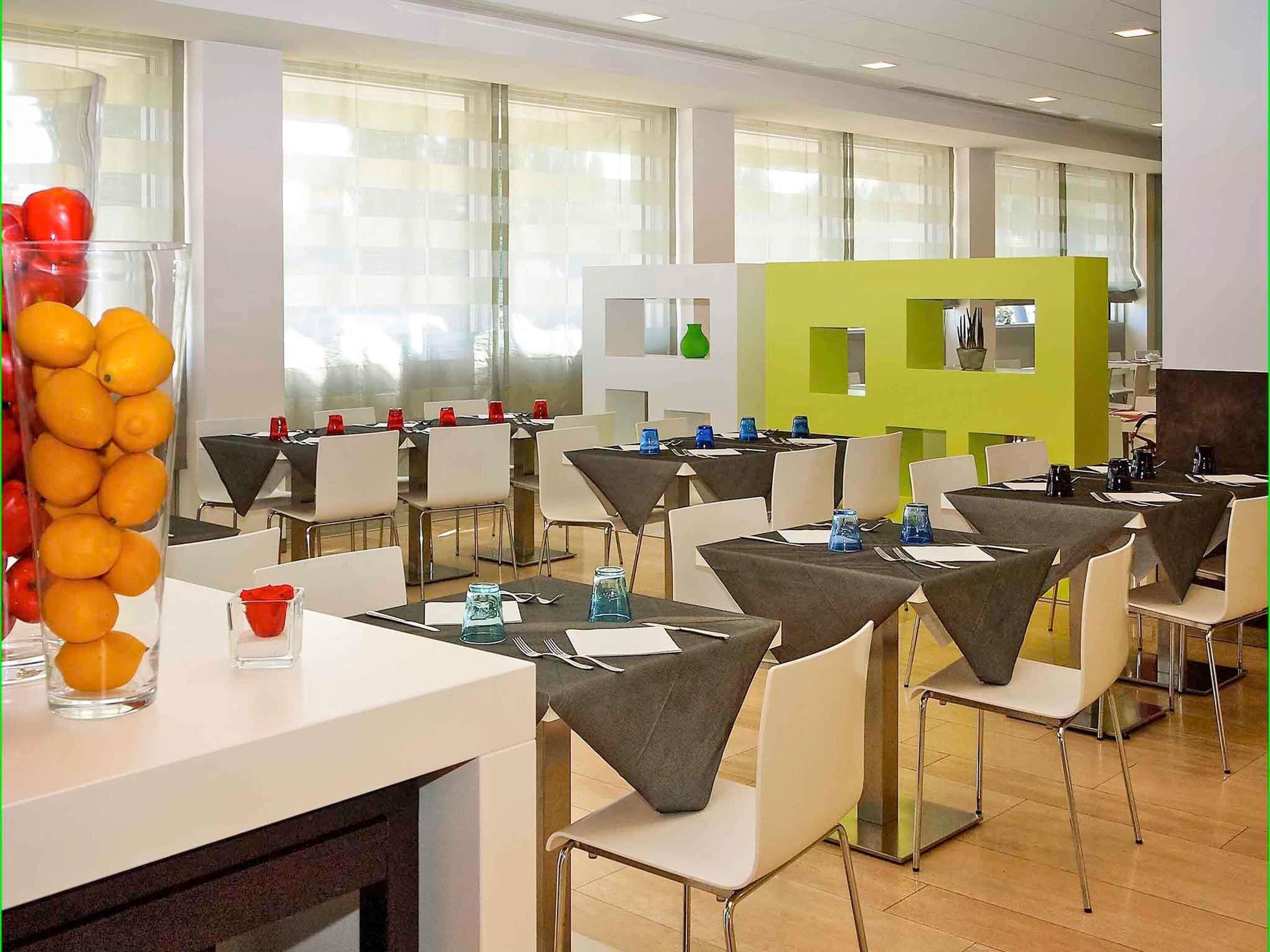 A modern dining area with tables set for a meal, a glass display of oranges, and a green partition.