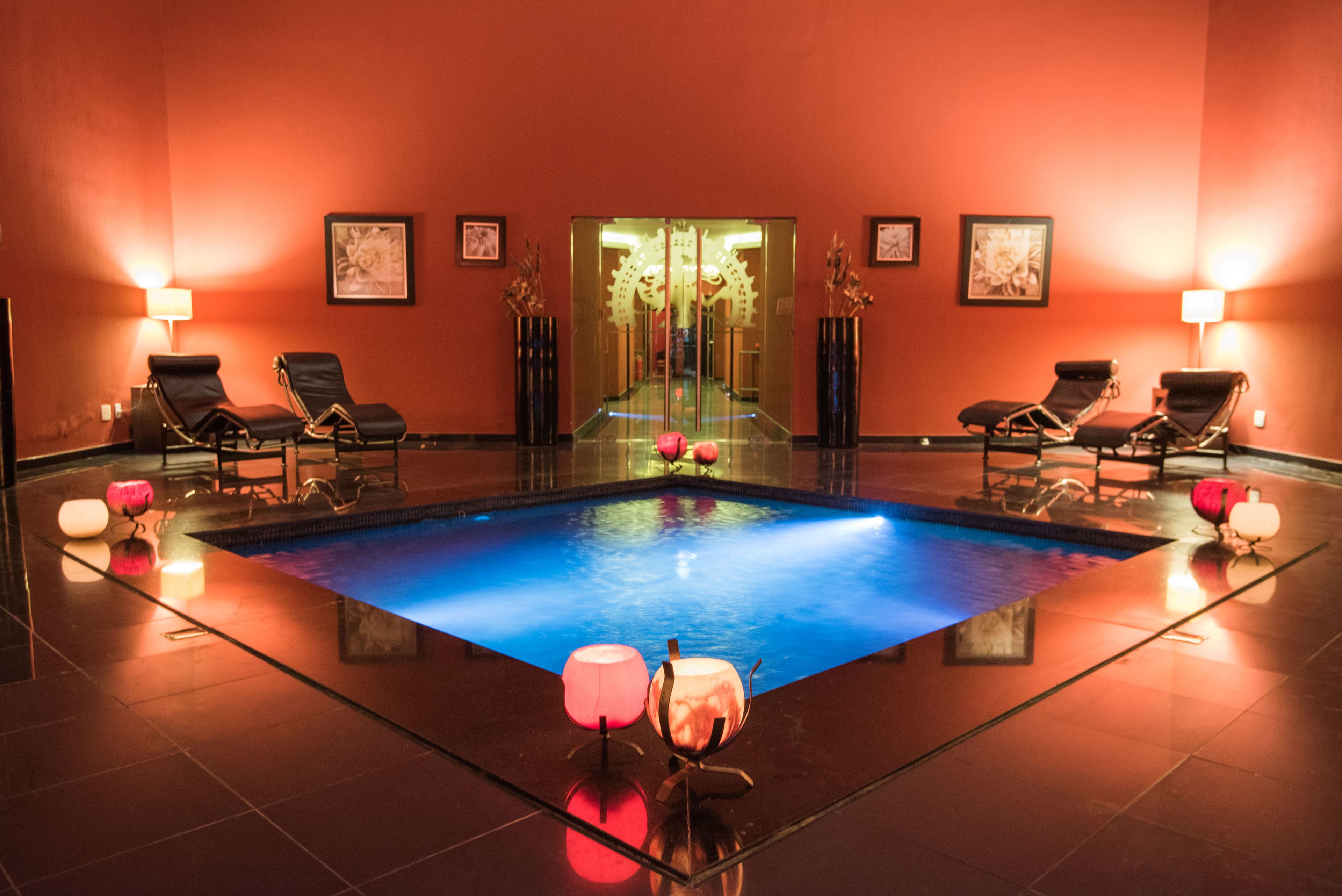 Uma área de spa com piscina, espreguiçadeiras e luminárias na parede.