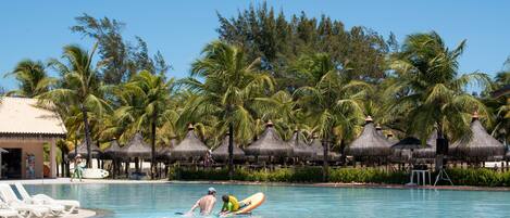 A swimming pool with lounge chairs, palm trees, and thatched-roof structures.