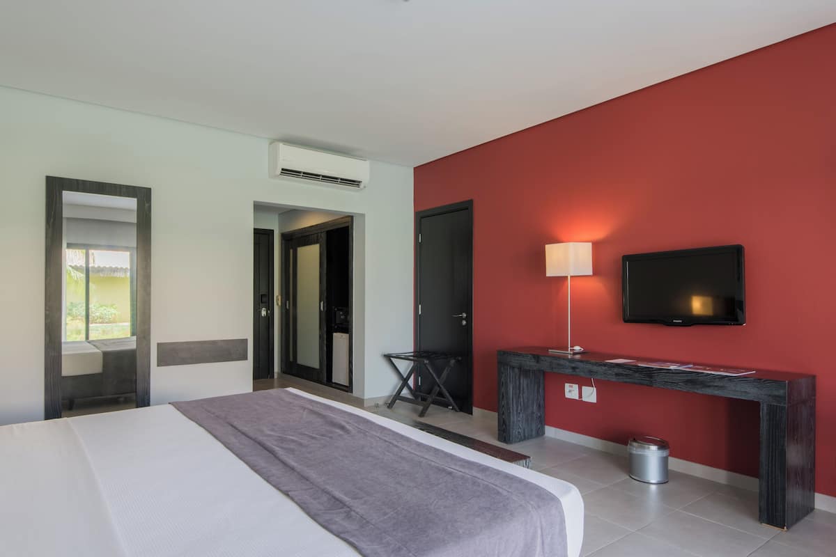Een hotelkamer met een bed, een bureau met lamp, een televisie en een airconditioning.