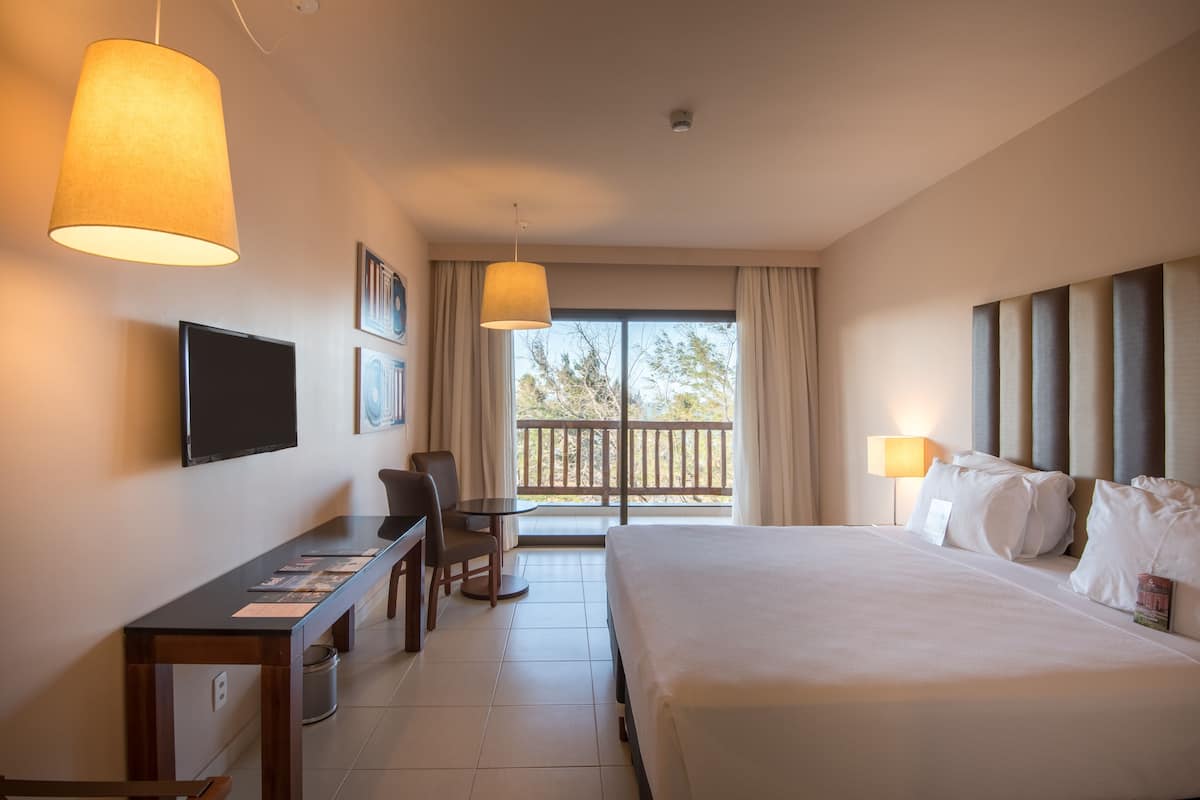 Een hotelkamer met een groot bed, een bureau met stoel, een televisie en een balkon met gordijnen.