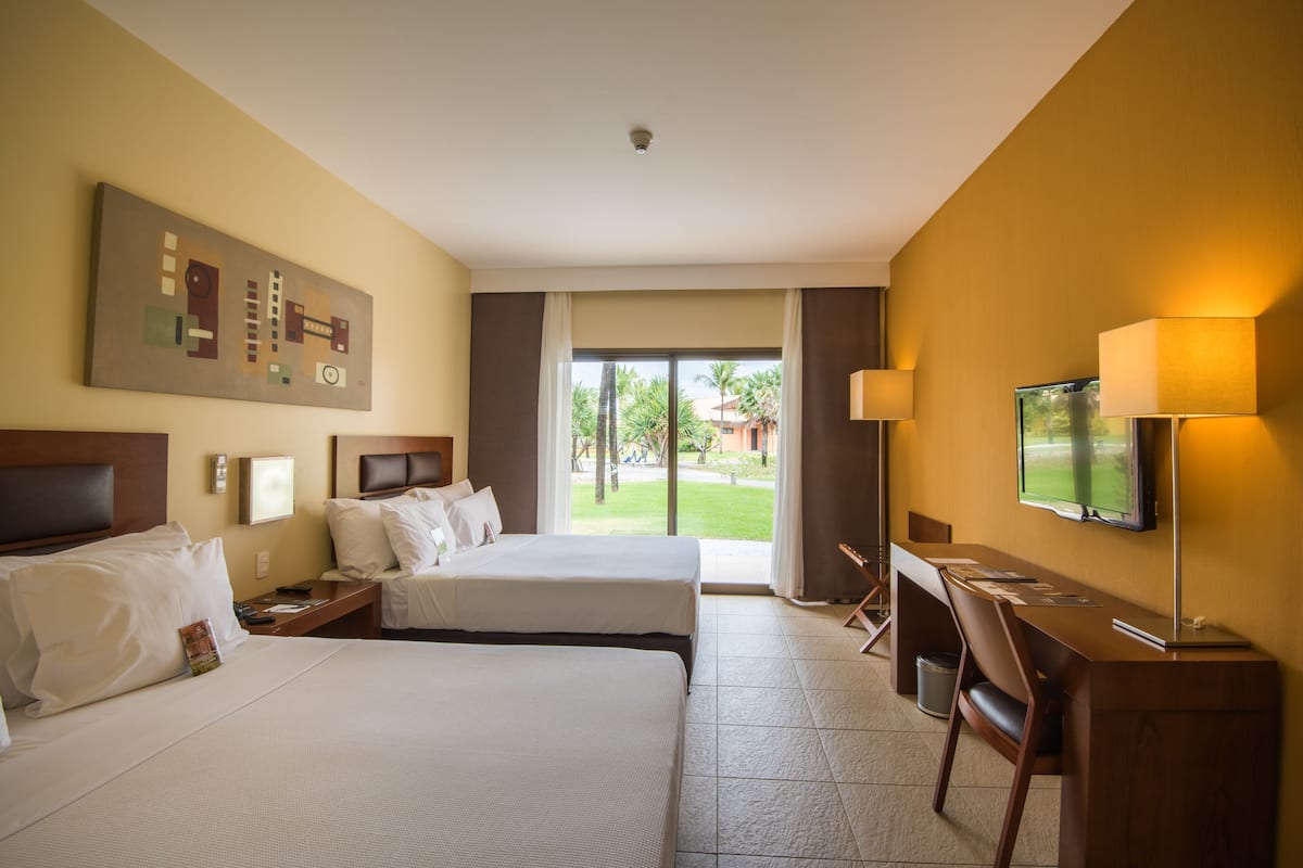 Een hotelkamer met twee bedden, een bureau, een televisie en uitzicht op de omgeving.