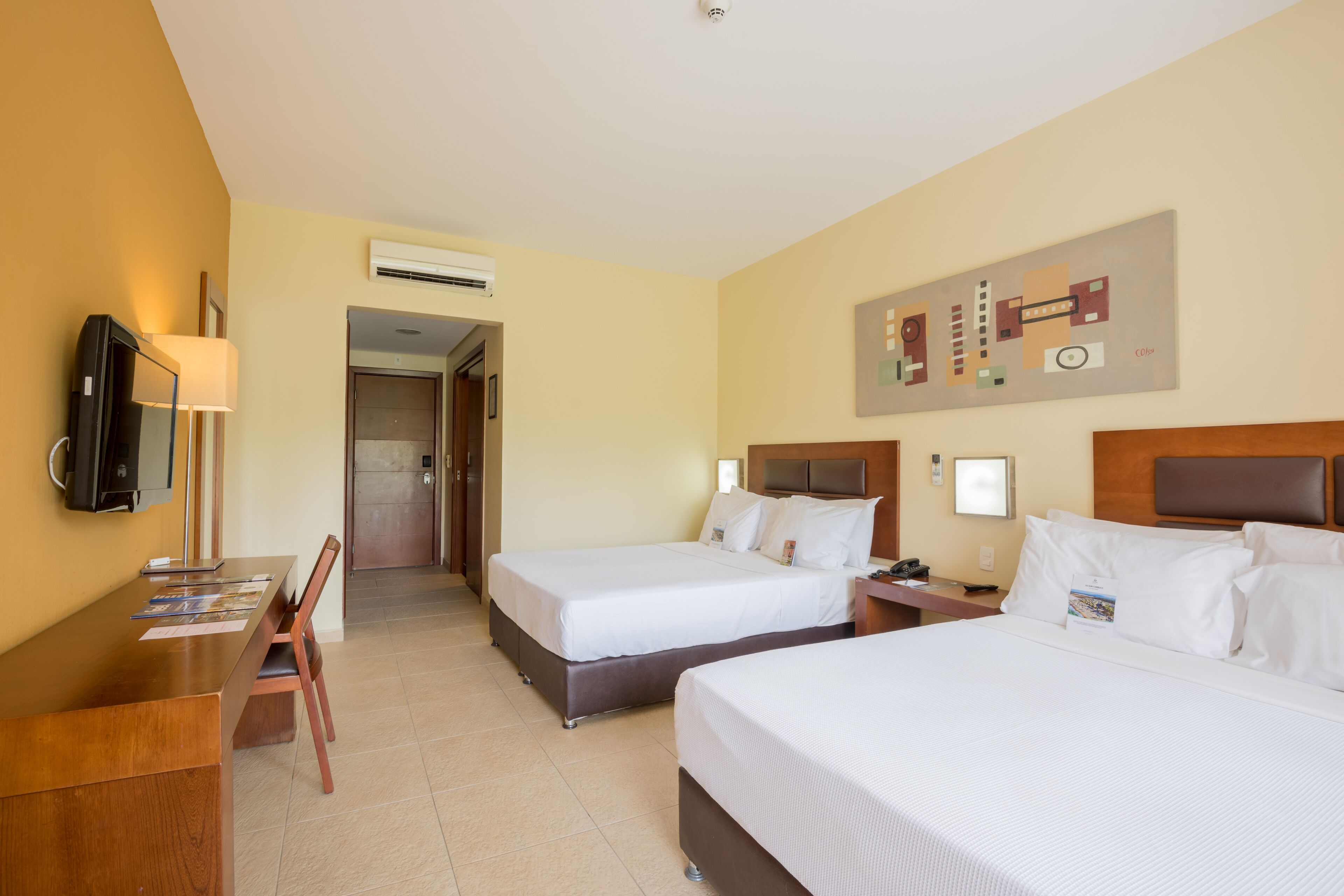 Camera d'albergo con due letti, una scrivania con una sedia, una televisione e un quadro appeso al muro.