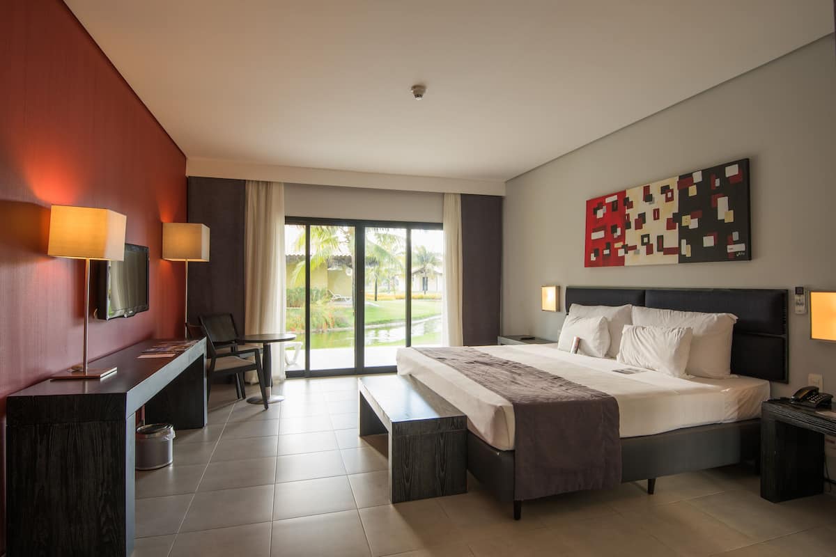 Een moderne hotelkamer met een groot bed, een bureau met computer, een televisie en uitzicht op het groen.