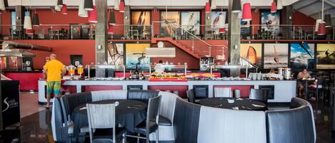 Un ristorante moderno con un'ampia zona bar, diverse aree salotto e una scala che conduce a un livello superiore.