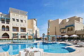 Ein Hotel mit Schwimmbad, Sitzgelegenheiten im Freien und blauem Himmel.