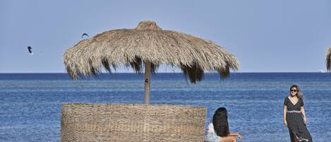 A beach scene with a thatched umbrella and a wicker chair.